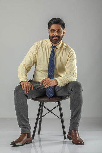 Portrait of handsome mid adult businessman posing confidently while sitting on stool against white background