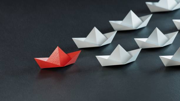 istock Leadership concept. Red leader paper ship leading among white on black background.3D rendering on black background. 1629327749