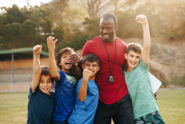 school kids celebrating with their coach on a sports field - soccer child coach childhood imagens e fotografias de stock