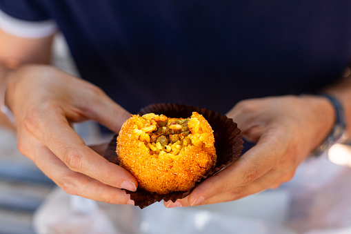 A man eating arancini, italian rice ball al ragu or al sugo, that is stuffed  with meat, peas and tomato sauce and spices, coated with breadcrumbs and deep fried. Sicilian street food, cuisine.
