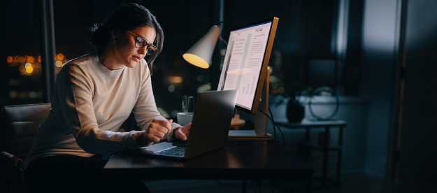 Caucasian woman works late from her home office, typing her ideas on her laptop. Professional business woman working late hours, maintaining a work-life balance and excelling in digital marketing.