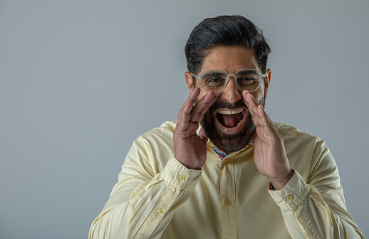 Portrait of handsome mid adult man with hands covering mouth shouting in anger while standing against white background