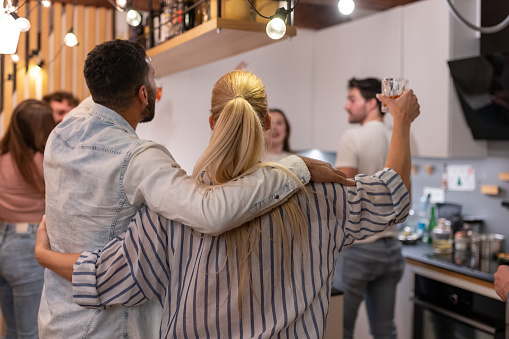 Two generations have a party at home with their partners, friends celebrate, sing, dance to music, sing karaoke on a mobile phone, have fun, drink alcoholic and non-alcoholic drinks. Girlfriends happily hug each other while dancing. A multi-racial society.