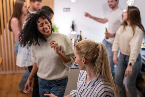 Two generations have a party at home with their partners, friends celebrate, sing, dance to music, sing karaoke on a mobile phone, have fun, drink alcoholic and non-alcoholic drinks. Girlfriends happily hug each other while dancing. A multi-racial society.