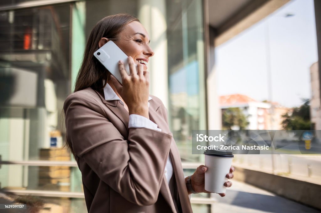 Focused and Caffeinated Businesswoman drinking coffee and using mobile phone in front of the office outdoor 30-34 Years Stock Photo