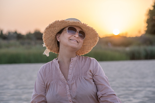 Young cheerful woman on a deserted beach at sunset. She looks at the camera through her sunglasses.