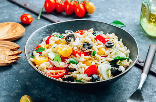 Mediterranean orzo salad with black olive, basil, red onion, tomato and cucumber. Summer pasta salad in gray bowl. Healhty food. Old galvanized table. Selective focus