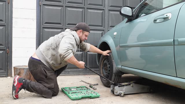 The professional auto mechanic uses a car jack while repairing the left wheel.