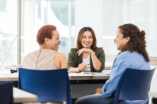 A multiracial group of businesswomen smile and talk during a staff meeting.