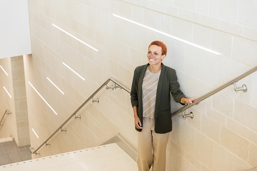 The smiling mid adult female high school principal stands in the stairwell at the school.