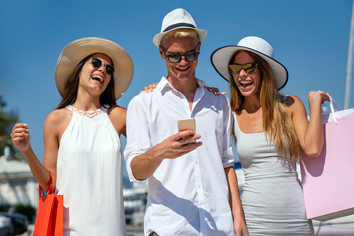 Vacation, travel, technology, smart phone, friendship and people concept. Smiling friends having fun, enjoying shopping