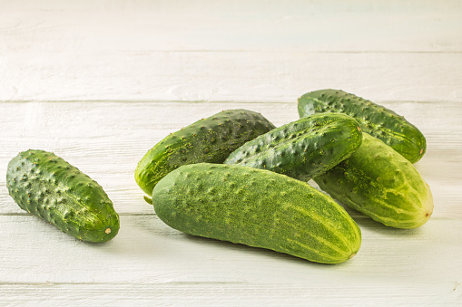 A bunch of fresh cucumbers with pimples on a white wooden table.