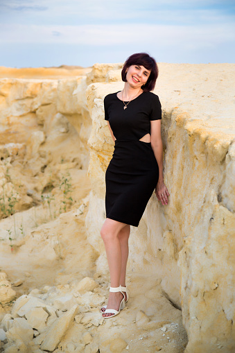 Girl in a black dress smiling on the edge of a cliff.