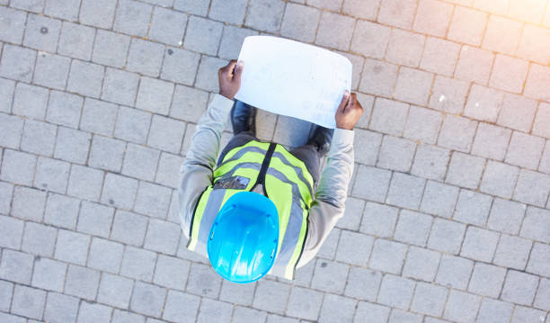 istock Man, architect and blueprint above for construction, planning or project ideas on site. Top view of male person, engineer or contractor with floor plan, documents or paper for building architecture 1629441571