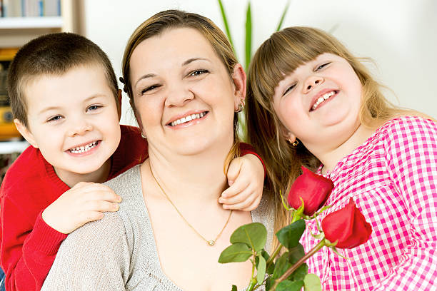 happy mother in the arms of his beloved children who gave her the most beautiful holiday red roses
