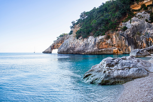 Crystal clear water laps the Cala Goloritzé, a cove of white small pebbles protected by a rugged cliff with a natural arch