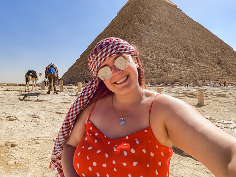 Beautiful young woman taking selfies in front of the Pyramids of Giza (Egyptian pyramids) in Cairo, Egypt.