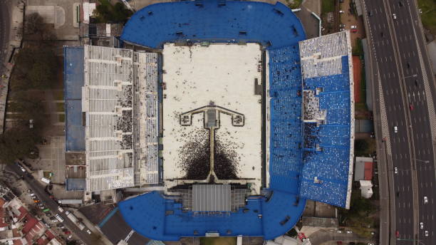 Aerial view on crowded tribune, American football stadium with team on filed. Open air arena with blue sunny sky. Daytime competition. Professional sport, event, tournament, game, championship concept