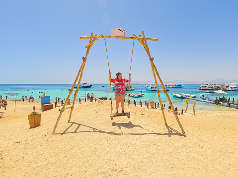 Beautiful young plus size woman swinging on the swing on the beach on the Paradise island in Egypt.