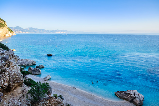 Crystal water laps Cala Goloritzé, a cove protected by a rugged cliff reachable via trekking among Mediterranean scrub in the Supramonte di Baunei