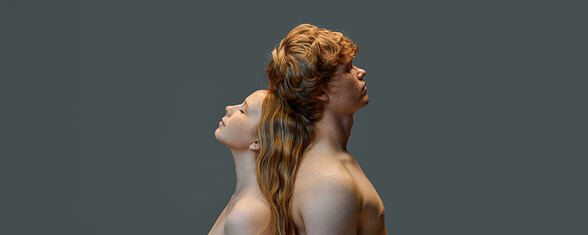 Fashionable attractive redhead couple, handsome man and beautiful woman with bare shoulders standing back to back in the studio. Concept of natural beauty, love, relationships, fashion. Ad. Banner