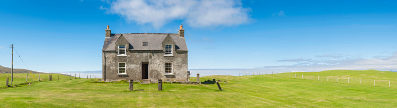 Charming country cottage in an idyllic rural location of vibrant green fields and blue panoramic skies overlooking the picturesque coastline beyond. ProPhoto RGB profile for maximum color fidelity and gamut.