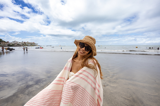 Portrait of happy woman in blanket standing on summer beach