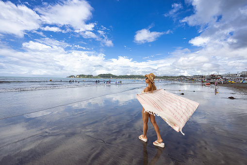 Woman in bikini wearing blanket and walking on summer beach - wide view