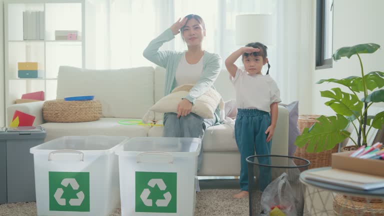 Young Asian family mom teaching kid how to recycle help the girl aware environmental importance and smiling looking at camera in living room at home. Family happy moment.