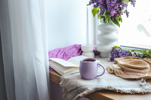 istock Cup of tea, straw hat, open book and lilac basket, spring still life 1629505610