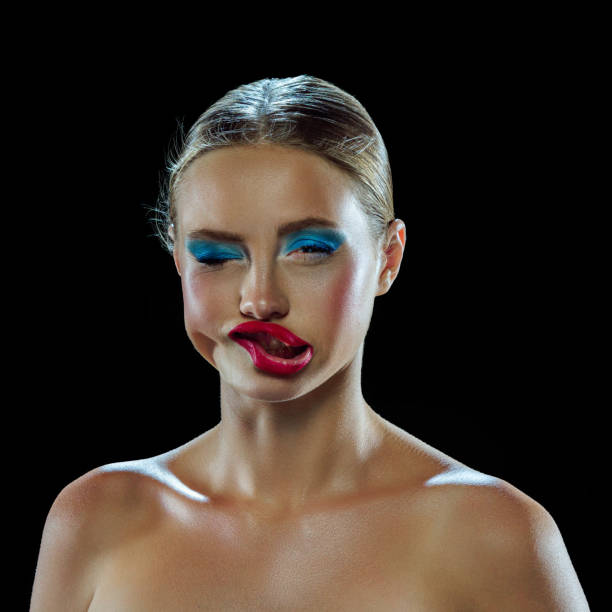Strong wind blowing on beautiful girl's face with bright colorful make-up, distorting face isolated black mode background. Funny emotion. Concept of holiday, celebration, cosmetic, fashion and beauty.