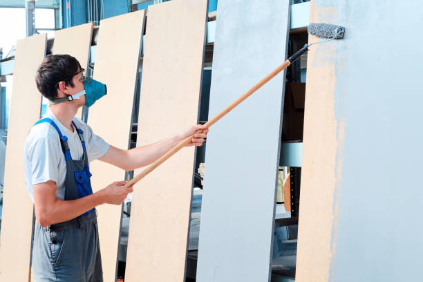 istock Painter in respirator and overalls paints wooden boards with paint roller on long handle. Worker paints shelving unit grey 1629509296