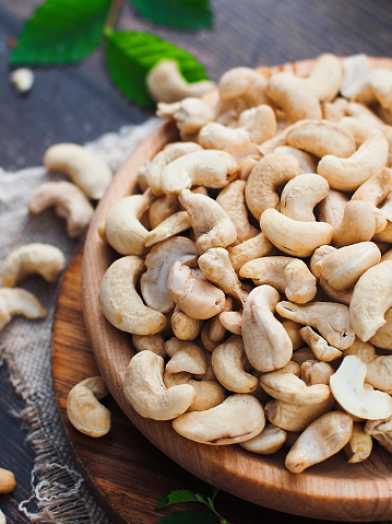 Cashew nuts are poured into wooden plate on table. Close-up still life. Advertising photo for sale of shelled cashews. Background.