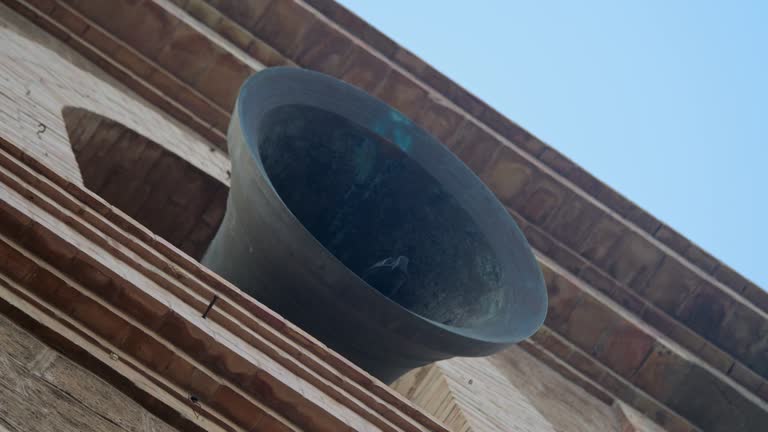 Historic bell in motion atop a tower, sounding its tone with a counterweight in view.