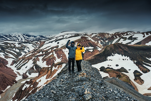 Achievement of young asian hiker couple standing on destination of Blanhjukur trail among volcanic mountain on highland in summer at Landmannalaugar, Iceland