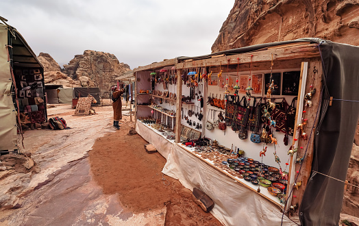 Petra, Jordan - January 20, 2020: Souvenirs stalls with unknown Bedouin shopkeeper in distance. Rocky landscape typical for this area background