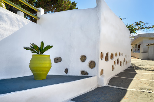 Stylish Mediterranean alleyway or street, classic whitewashed walls, stone pavement, decorative golden vase with palm sprout. Minimalistic design based on classic features of Greek traditions. Fusion, eclectic elements. Milos, Greece