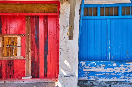Colorful blue and red boat garage doors in Klima fishermen village, Milos island, Greece. Traditional whitewashed house walls, painted, faded and weathered wooden doors and doorways, sunny summer day, authentic architecture and details. Frontal shot