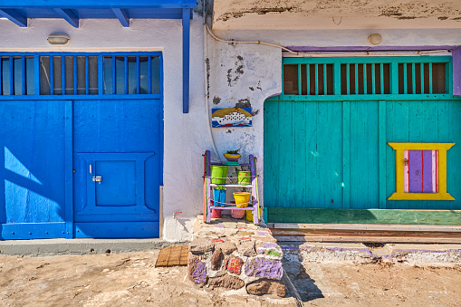 Colorful blue and green boat garage doors in Klima fishermen village, Milos island, Greece. Traditional whitewashed house wall, painted, faded and weathered wooden doors and doorways, sunny summer day, authentic architecture and details. Frontal shot