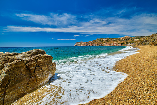 Sunny summer day on pebble and sandy beach Paleochori beach, Aegean sea, Milos island, Cyclades, Greece. Slow motion. low tide, waves, white sea spray, blue sky, azure sea waters, rocky hills and lonely rock. Perfect vacations location.