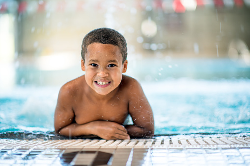 A young boy of African decent, rests at the edge of a community pool as he attends a swimming lesson.