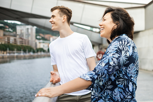 Happy couple is hugging, enjoying the seaside view and smiling while sitting on pier at the sea