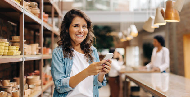 istock Cheerful young woman using a smartphone in her ceramic store 1629577425
