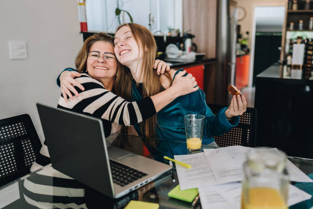 grandmother and granddaughter embracing at home - grandparent using computer laptop dining table zdjęcia i obrazy z banku zdjęć