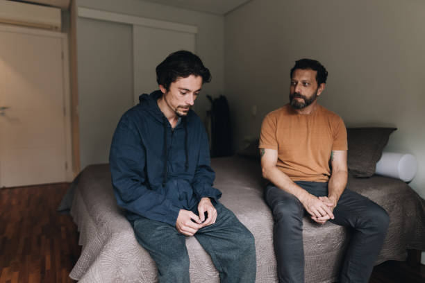padre hablando con su hijo triste en la cama de su casa - avergonzamiento fotografías e imágenes de stock