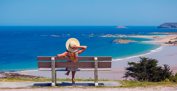 Woman sitting on a bench looking at atlantic ocean - vacation, travel destination, relaxing, summer holiday ( brittany in France)