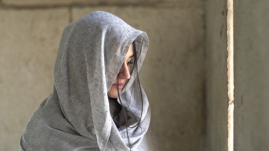 A beautiful young Persian woman wearing a veil while looking through the opening slit of a wall