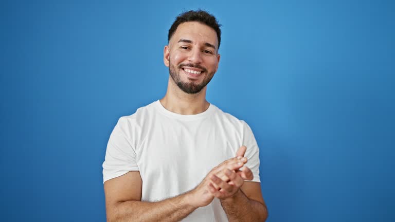 Young arab man smiling confident clapping hands over isolated blue background