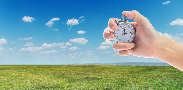 Human hand holding stopwatch on green grass