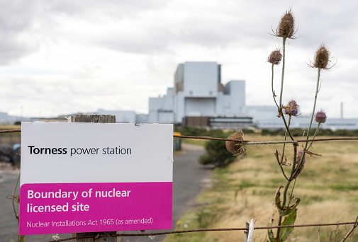 A sign denoting the boundary to Torness nuclear power station in the UK, with the power station exterior in the background.